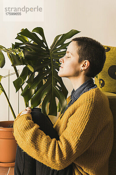 Woman with eyes closed sitting by monstera plant at home