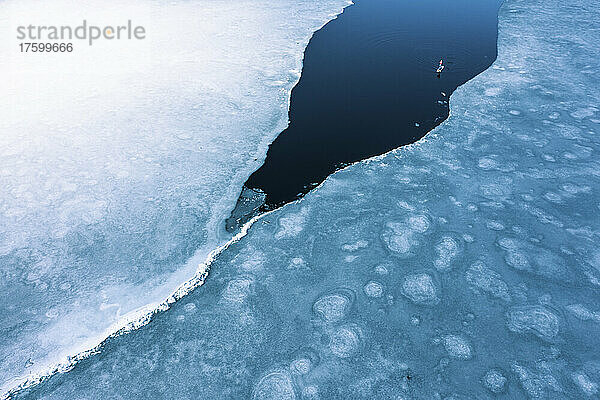 Germany  Bavaria  Aerial view of lone man paddleboarding between ice floes in Eibsee lake