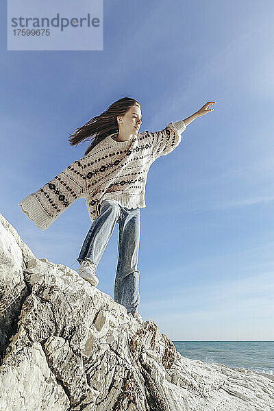 Carefree teenage girl balancing on rock at beach