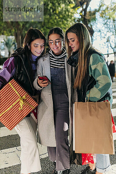 Junge Freunde mit Einkaufstüten teilen sich ihr Smartphone auf der Straße