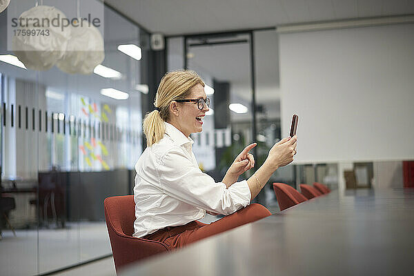 Glückliche Geschäftsfrau bei Videoanruf über Smartphone im Büro
