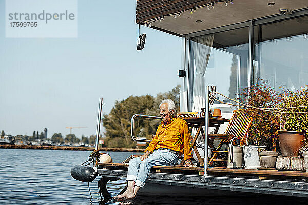 Fröhlicher älterer Mann sitzt an einem sonnigen Tag am Hausboot