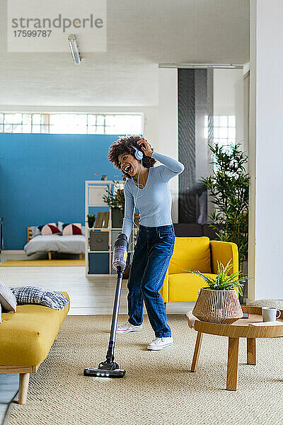 Fröhliche junge Frau genießt Musik und putzt Teppich im Wohnzimmer