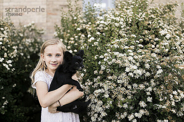 Blondes Mädchen mit Hund an einer weiß blühenden Pflanze