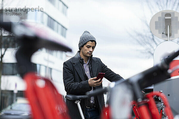 Mann benutzt Smartphone  um am Parkplatz ein Fahrrad zu mieten