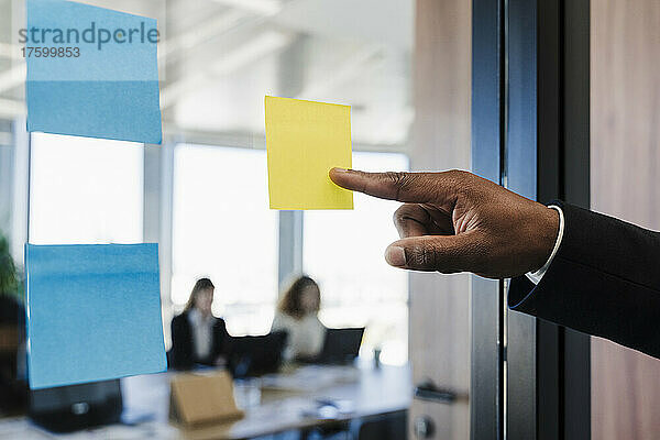 Geschäftsmann zeigt auf Klebezettel an Glaswand im Coworking-Büro