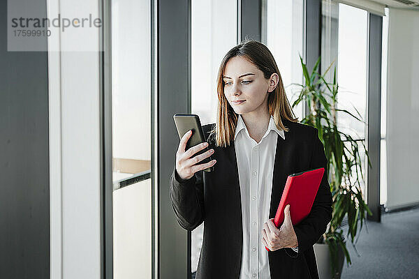 Geschäftsfrau nutzt Smartphone und hält Tablet-PC im Büro