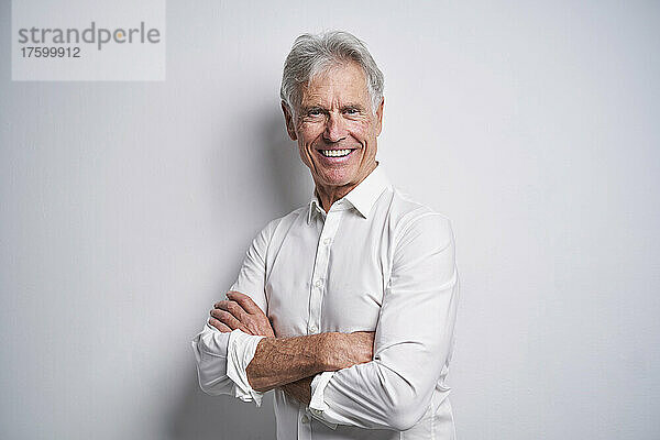 Smiling senior businessman with arms crossed in front of white background