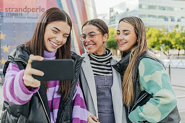 Smiling young women taking selfie on smart phone in city
