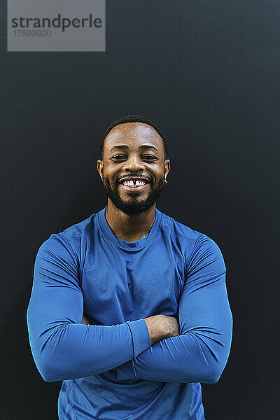 Smiling athlete with arms crossed against black background
