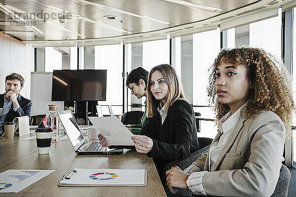 Junge Geschäftsfrauen sitzen mit Kollegen am Konferenztisch im Sitzungssaal