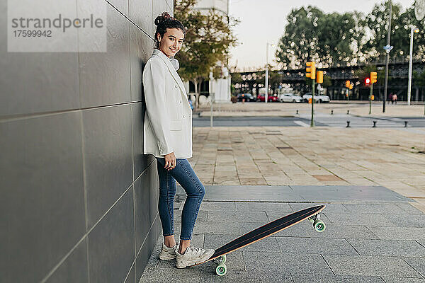 Lächelnde junge Frau mit Skateboard auf Fußweg