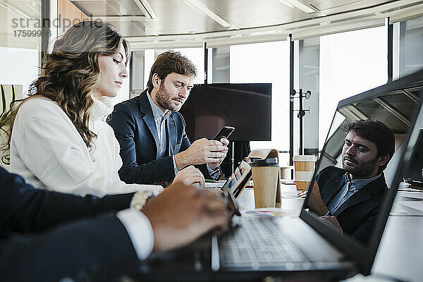 Geschäftsmann benutzt Smartphone und sitzt neben Kollegen  die am Schreibtisch arbeiten