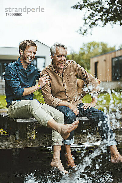 Glücklicher Vater und Sohn sitzen auf dem Steg und spritzen Wasser im Hinterhof