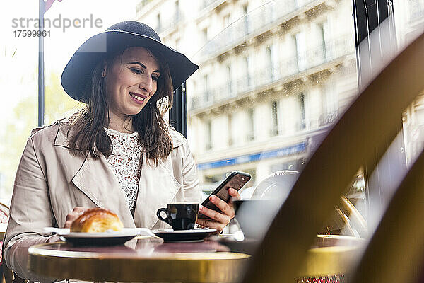 Lächelnde Frau benutzt Mobiltelefon im Café