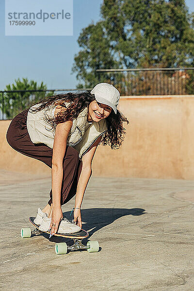 Lächelnde Frau  die an einem sonnigen Tag im Park Skateboard fährt