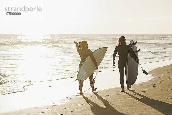 Frauen mit Surfbrettern gehen bei Sonnenuntergang am Strand spazieren  Gran Canaria  Kanarische Inseln