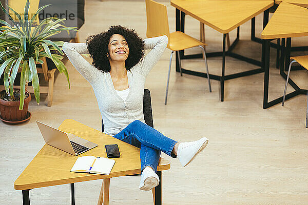 Happy businesswoman with hands behind head in creative office