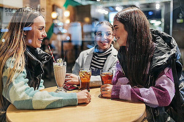 Junge Frauen mit Getränken am Tisch unterhalten sich im Café