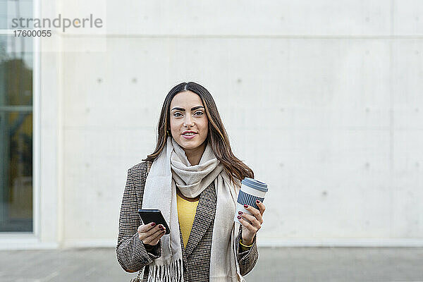 Junge Frau mit Smartphone und wiederverwendbarer Kaffeetasse auf Fußweg