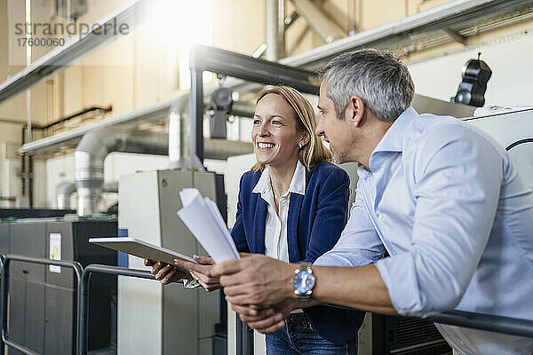 Lächelnde blonde Geschäftsfrau mit Tablet-PC steht ihrem Kollegen in der Fabrik zur Seite