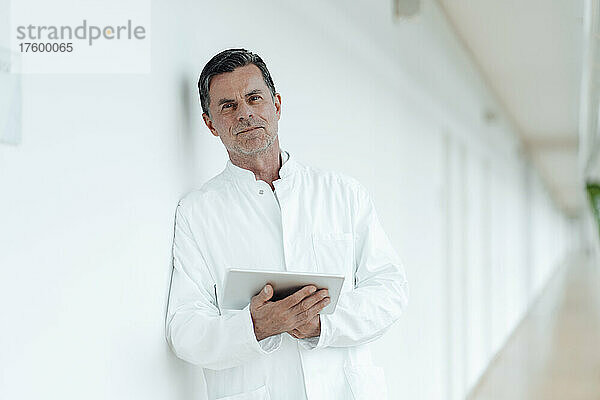 Wissenschaftler mit Tablet-PC lehnt an Wand in medizinischer Klinik