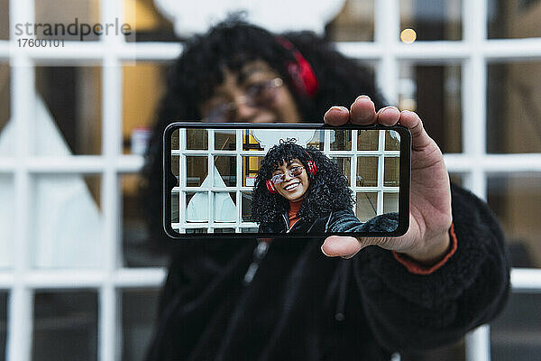Cheerful woman taking selfie through smart phone