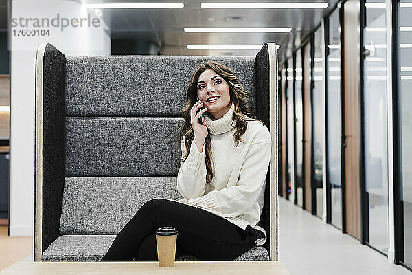 Geschäftsfrau spricht am Smartphone und sitzt am Sitz im Büro