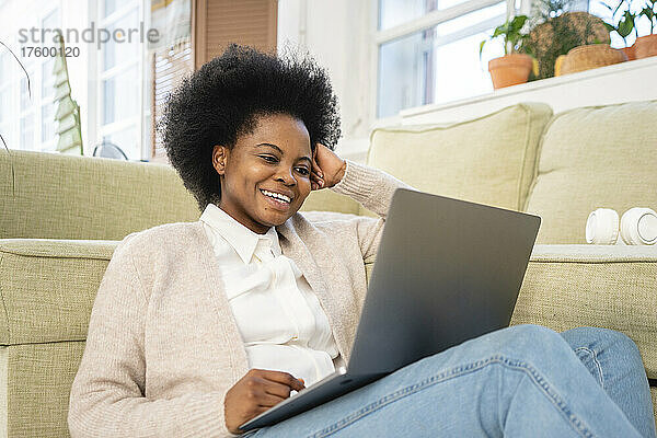 Glücklicher Freiberufler  der zu Hause im Wohnzimmer einen Laptop neben dem Sofa nutzt
