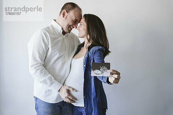 Glückliches Paar zeigt Ultraschalluntersuchung an der Wand