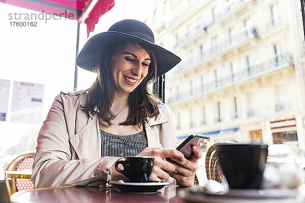 Glückliche junge Frau mit Smartphone sitzt im Café  Paris  Frankreich