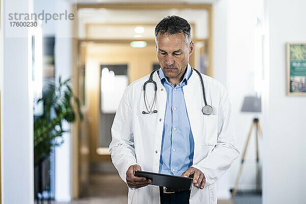 Reifer Arzt untersucht Krankenakte auf Tablet-PC im Krankenhaus