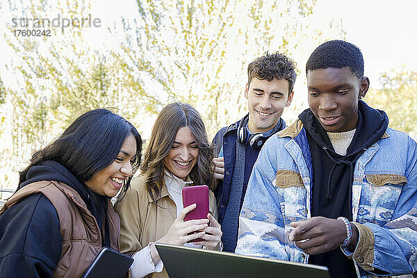 Fröhliche Studenten mit Smartphone und Laptop auf dem Campus