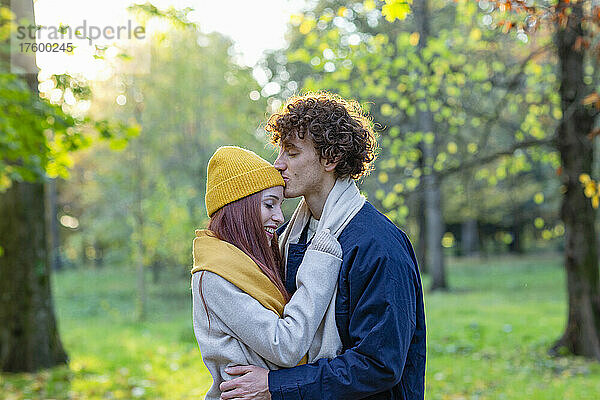 Junger Mann umarmt und küsst die Stirn seiner Freundin im Herbstpark
