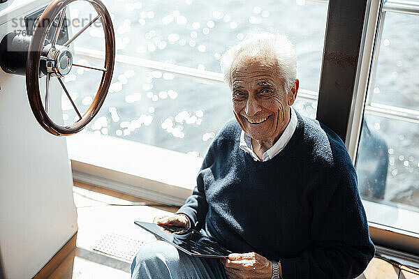 Glücklicher älterer Mann sitzt mit Tablet-PC am Hausboot
