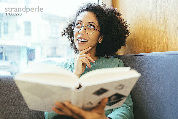 Nachdenkliche Frau mit Buch auf dem Sofa