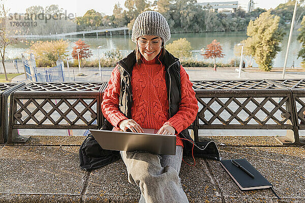 Junge berufstätige Frau sitzt mit Laptop und Tagebuch auf der Bank