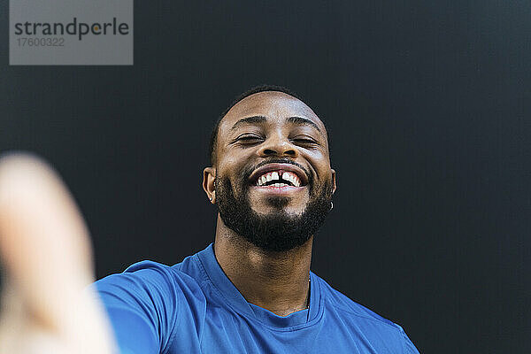 Cheerful athlete with gap teeth taking selfie against black background