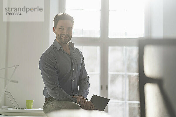 Selbstbewusster Geschäftsmann mit Tablet-PC sitzt im Büro