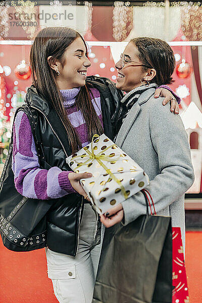 Fröhliche Freunde  die sich zu Weihnachten umarmen und ein Geschenk in der Hand halten