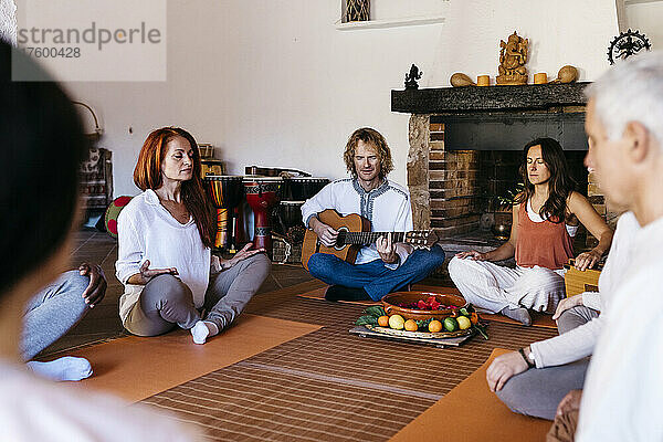 Musiker spielt Gitarre inmitten meditierender Freunde im Bauernhaus