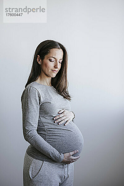 Schwangere Frau mit geschlossenen Augen steht vor der Wand