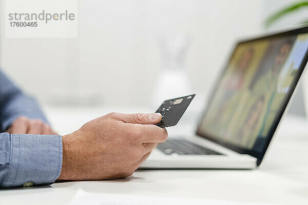 Geschäftsmann mit Kreditkarte bei Videoanruf über Laptop im Büro