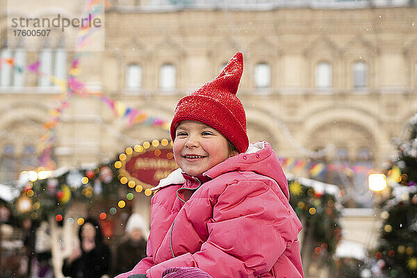 Lächelndes Mädchen mit Strickmütze auf dem Weihnachtsmarkt