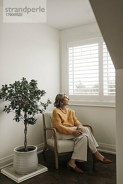 Frau sitzt auf einem Stuhl und schaut zu Hause durch das Fenster