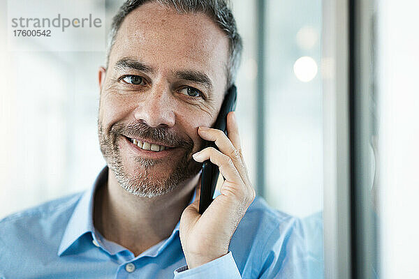 Lächelnder Geschäftsmann  der im Flur mit dem Handy telefoniert