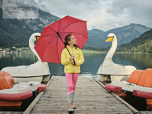 Mädchen mit Regenschirm läuft mit Tretbooten am Steg vorbei