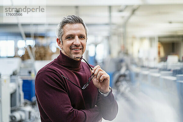 Lächelnder Geschäftsmann mit Brille in der Fabrik