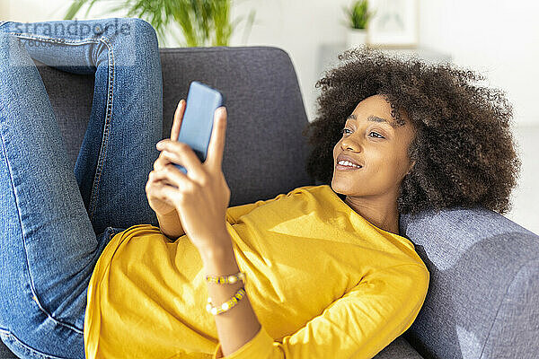 Junge Frau benutzt Smartphone und entspannt sich zu Hause auf dem Sofa