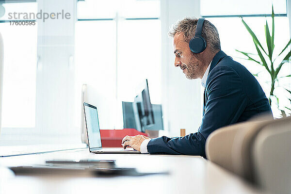 Geschäftsmann mit kabellosen Kopfhörern und Laptop am Schreibtisch am Arbeitsplatz